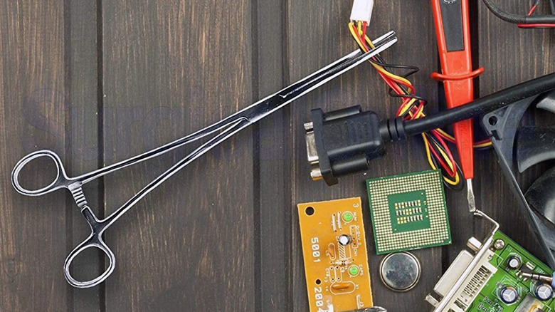 A pair of hemostats holding electrical wire with other things nearby