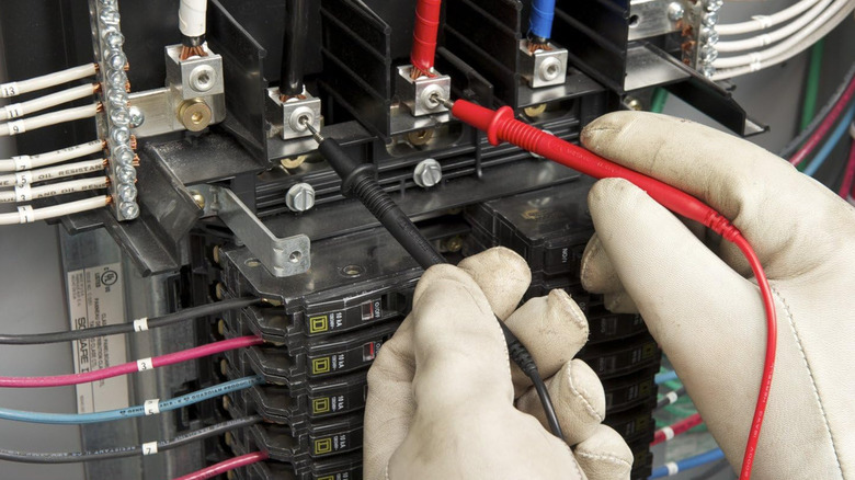 An electrician using a multimeter to test electrical flow on breaker box
