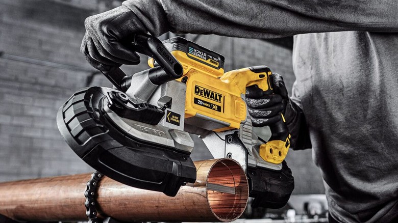 A construction worker sawing a piece of metal with a handheld band saw