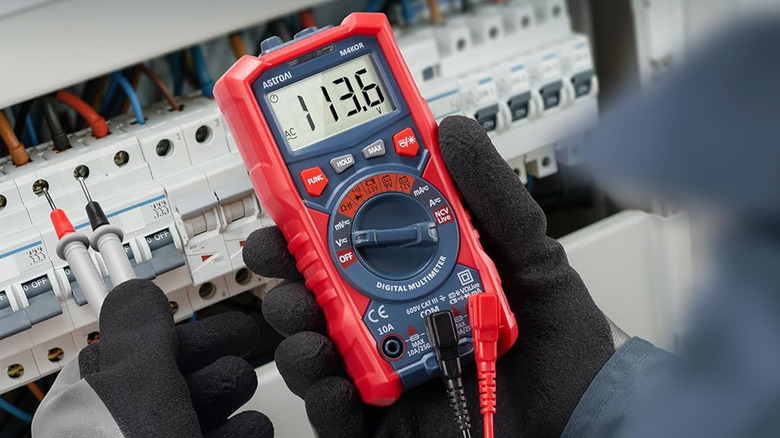 An electrician using a multimeter on a switchboard.