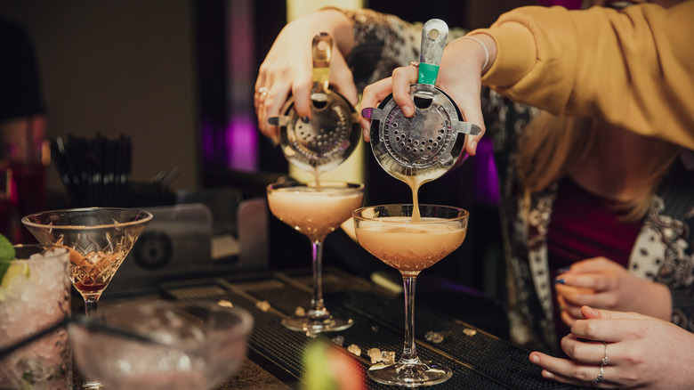 Two people pouring cocktails into separate glasses