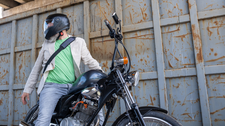 man in green shirt on parked motorcycle with helmet on looking back