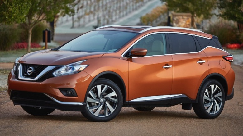 Orange 2016 Nissan Murano parked on a dirt road with trees in the background.