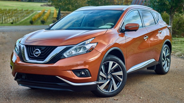 Orange 2016 Nissan Murano parked on a dirt road with trees in the background.