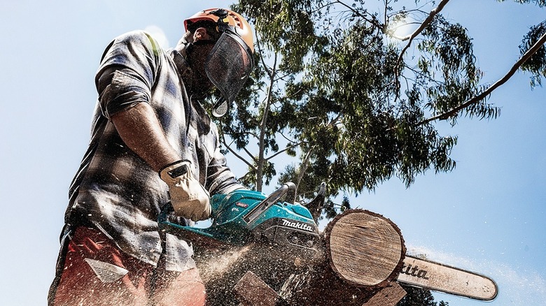 Person using chainsaw, wearing safety helmet