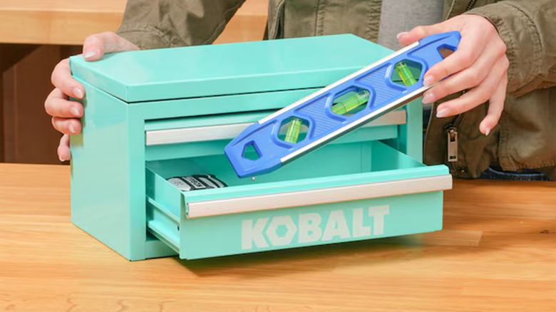 A woman putting a level into an aqua-colored mini toolbox