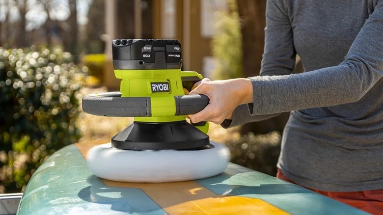 A person using a Ryobi buffer to wax a surf board