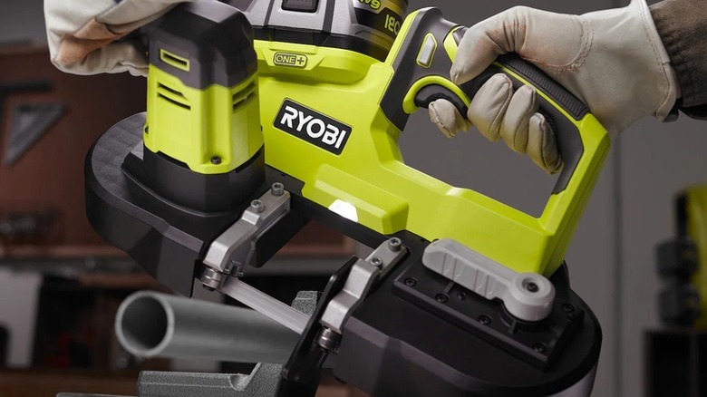 A person wearing safety gloves using a Ryobi compact band saw to cut a length of pipe.