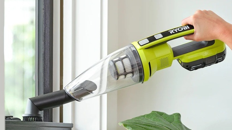 A person using a Ryobi hand vacuum to clean a windowsill