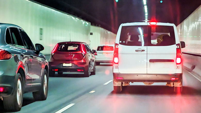 View from behind several vehicles driving through a tunnel, showing a white van on its brakes.