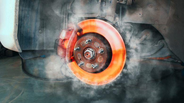 A car brake rotor glowing red-hot from heat, with smoke rising around it.