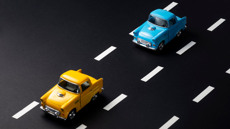 Toy yellow car and toy blue car on a black surface designed to look like a two-lane road with white dashed lines.