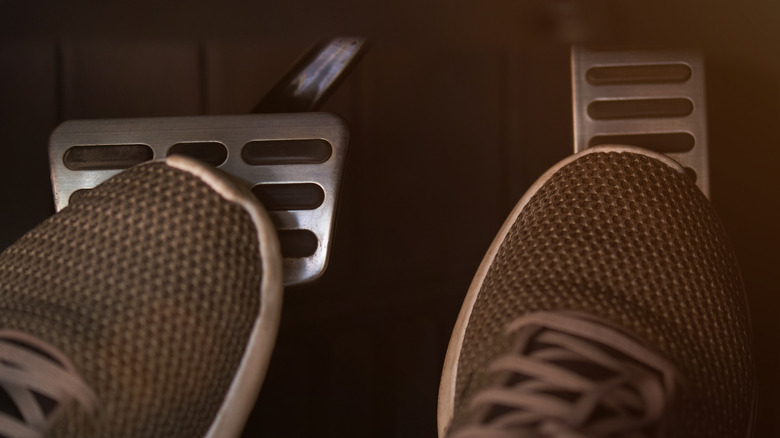 Close-up view of a driver's feet on car pedals, with one foot pressing the brake and the other on the gas pedal.