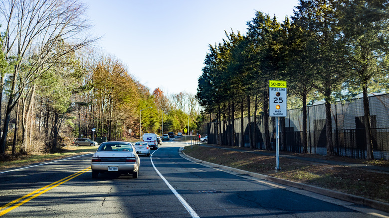Cars driving on a two-lane road past a school zone sign showing a 25 mph speed limit.