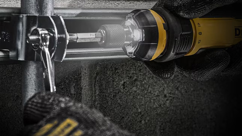 A person using a DeWalt electric screwdriver on a metal bracket