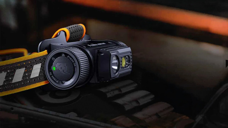 A Fenix headlamp on a dark table with orange backlighting