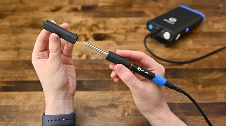 A person using an iFixit soldering iron on a wood table