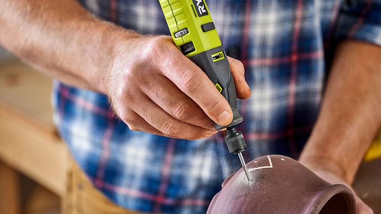 A man using a Ryobi rotary tool to carve into a clay pot