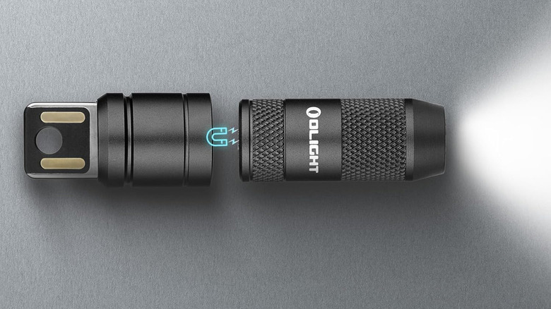An Olight iMini 2 flashlight on a gray surface with its charger