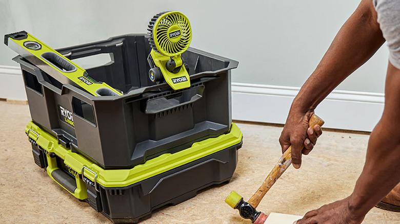 A person working on a floor with a Ryobi clamp fan nearby
