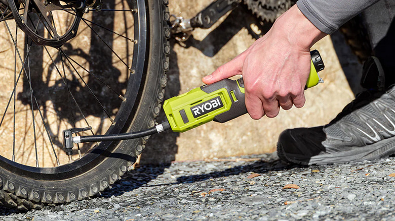 A person pumping up a bike tire with a Ryobi inflator