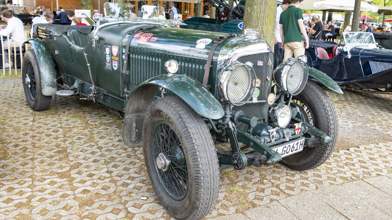 A 1930s Bentley 8 liter racing car on display to the public at an outdoor auto show, standing on paver stones.