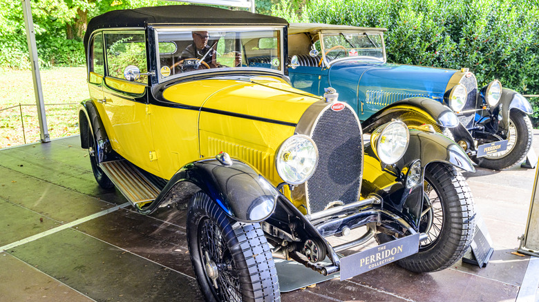 A pair of Bugatti Type 46s from the early 1920s on display under a covered tent at an outdoor show.