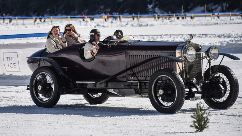 A black Hispano-Suiza H6C with four passengers moving at speed from left to right across a snow-covered surface.