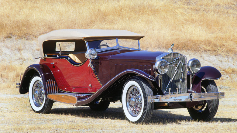 A 1933 Isotta Fraschini Tipo 8AS parked in a field, with its beige canvas roof up, finished in two-tone burgundy and red.