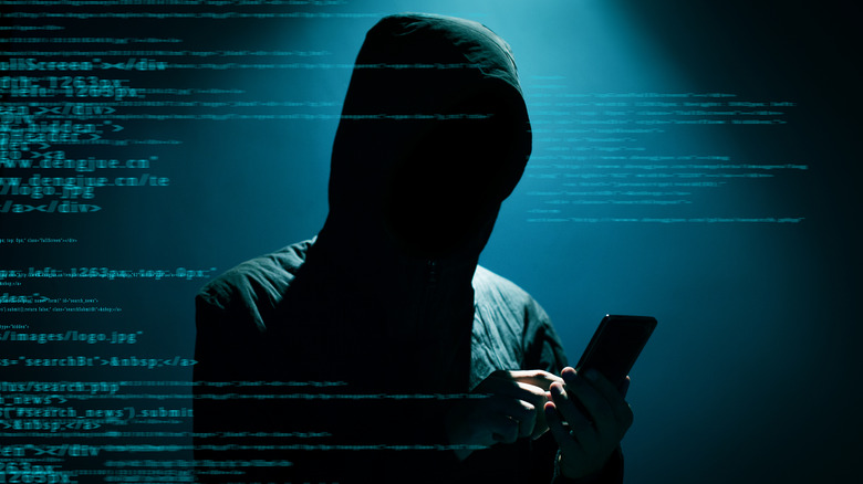 hooded hacker in the dark looking at phone