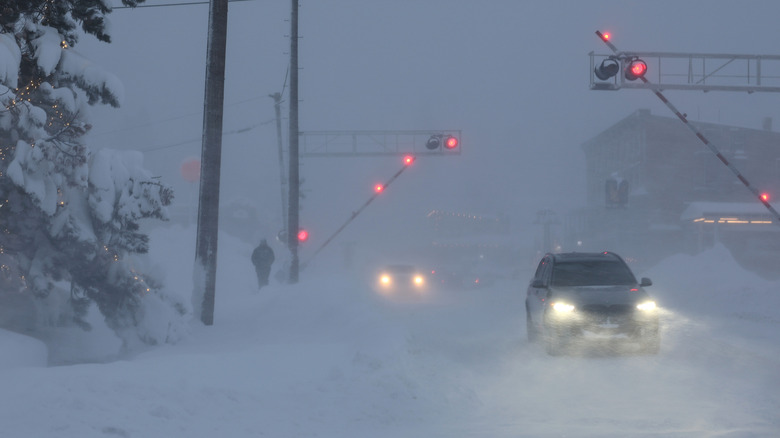 Cars drive in a heavy snowstorm near a railroad crossing