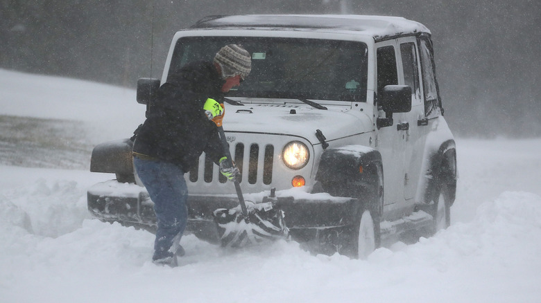 A man shovels out a 4x4 Jeep in deep snow