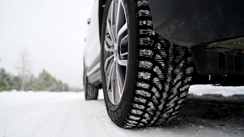 Close-up of right front wheel of car with snow tires on snowy road