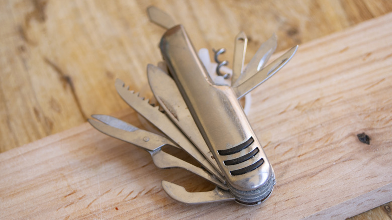 Silver multi-tool with all tools exposed while balancing on a piece of wood