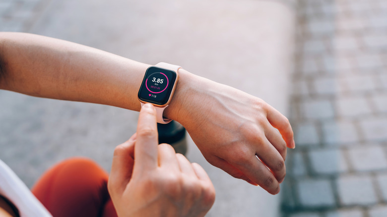 Over the shoulder view of young Asian sports woman checks her fitness statistics on smartwatch to monitor her training progress after working out in city outdoors.