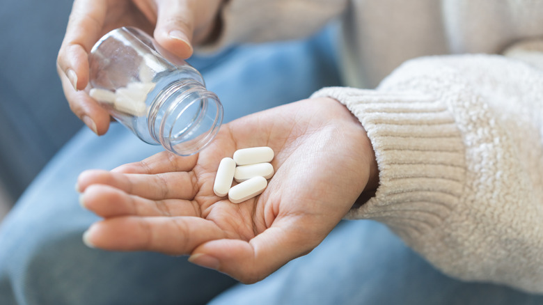 Sick asian young woman, girl holding tablet pill on hand pouring drug from medication bottle.