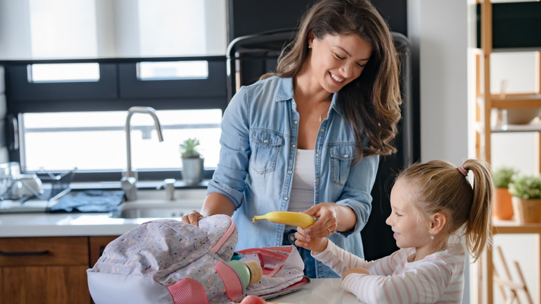 Woman packing a banana into a lunch box for a young girl