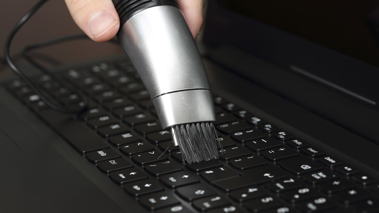 Hand holding a mini vacuum nozzle cleaning a computer keyboard