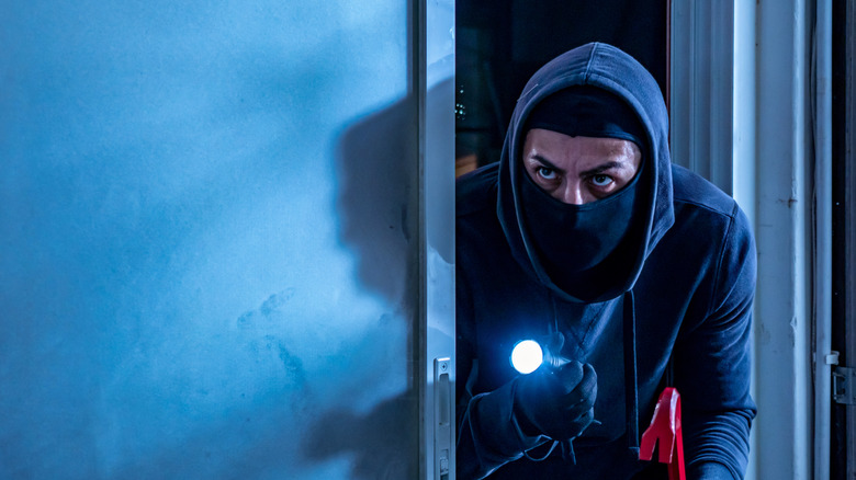 A man wearing a balaclava holding a flashlight sneaking around in a home