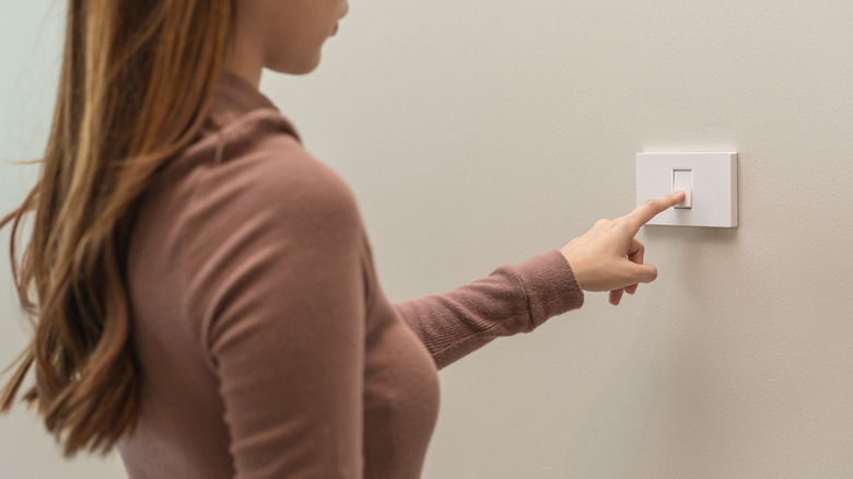 A woman using her finger to flip a wall switch