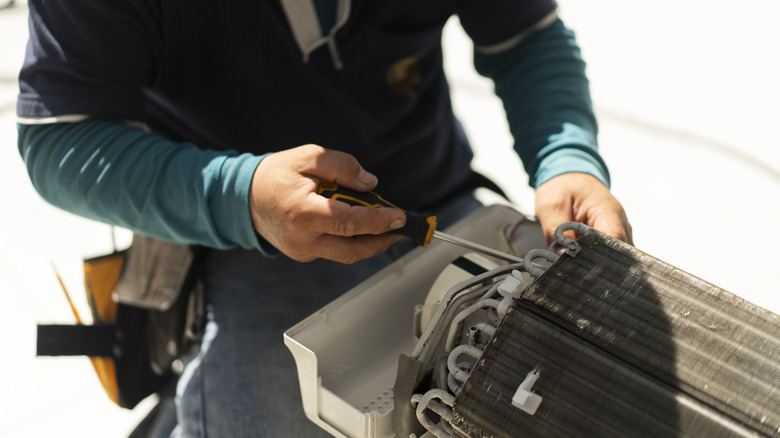 A person holding a screwdriver and working on an AC unit