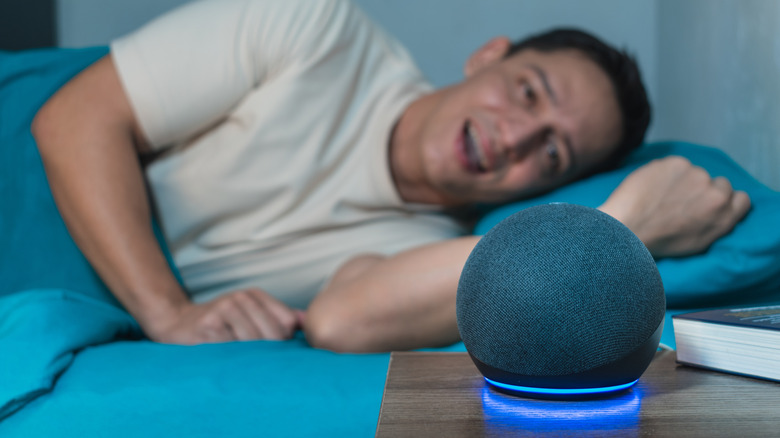 A man in bed talks to an Alexa device on a bedside table