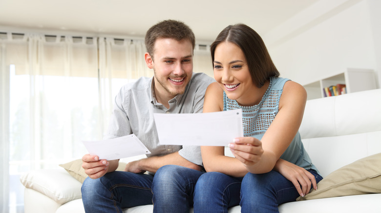 A couple holding a white paper bill while sitting on a couch smiling