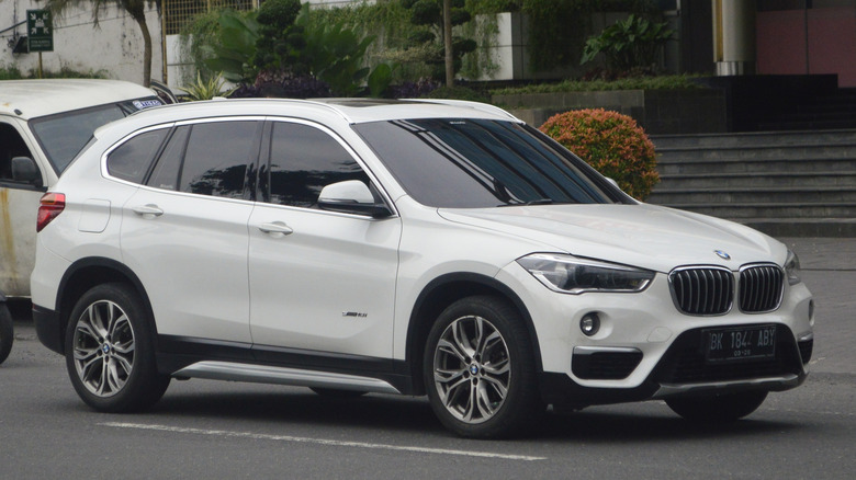 A white 2013 BMW X1 on the street in the middle of the day, with trees visible in the back