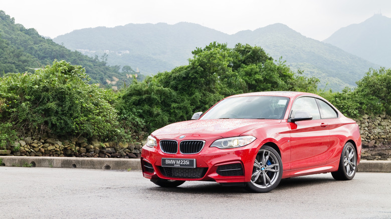 A red 2014 BMW M235i being photographed against a picturesque backdrop on a test run