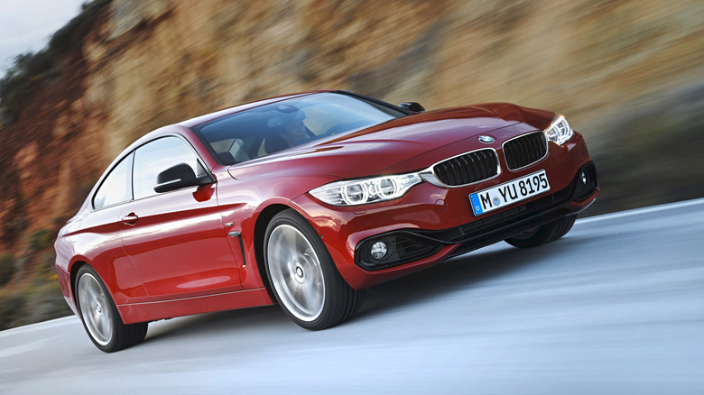 A red BMW 4-series car zooming along a road with a mountain to its right