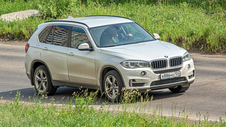 A white-colored BMW X5 on the F15 platform moving along a road in Russia