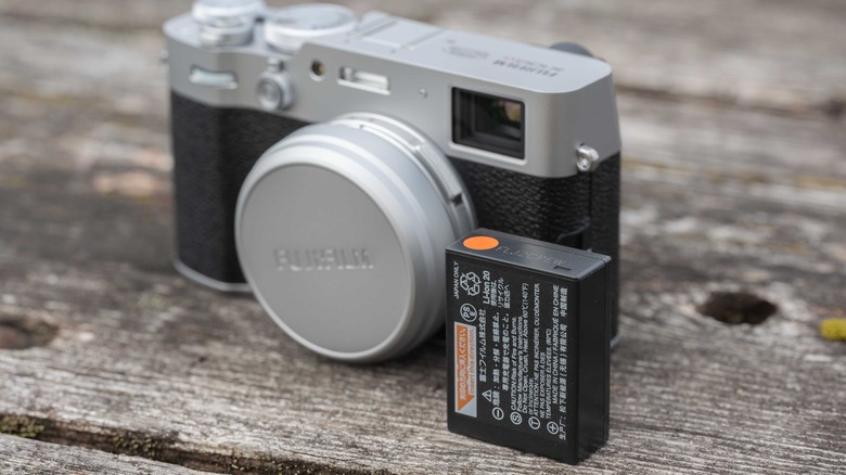 Battery next to the Fujifilm X100IV on a worn picnic table.