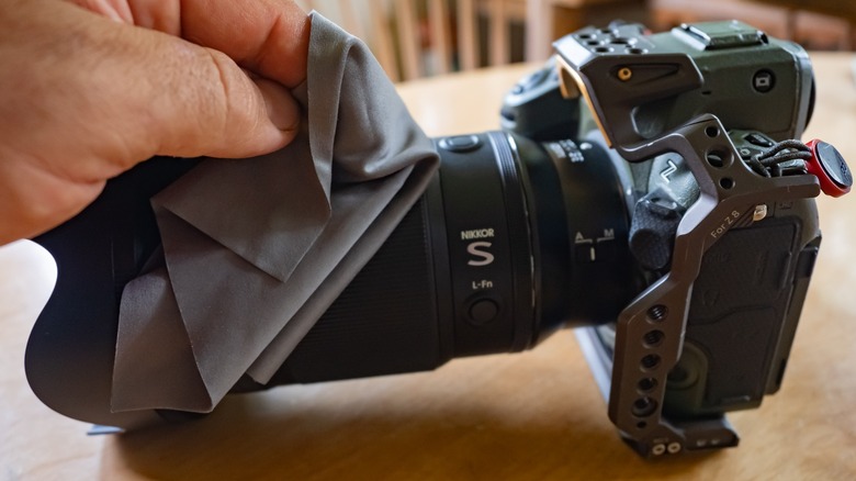 A hand wiping down the lens attached to the Nikon Z8 with a cloth.