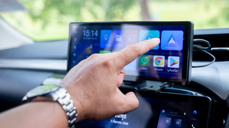 Hand touching a screen on a car dashboard
